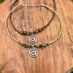 May include: Two layered necklaces with brown and beige cords, green and brown beads, and a silver spiral pendant.