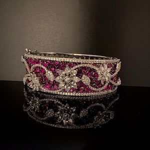 May include: A silver bangle bracelet with a floral design set with pink rubies and white diamonds.
