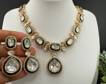May include: A gold necklace and earrings set with a green enamel design and clear stones. The necklace has a teardrop pendant.