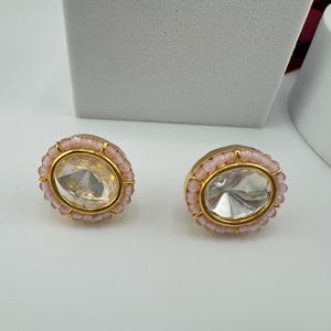 May include: A pair of gold earrings with a clear crystal center surrounded by a ring of pink beads.