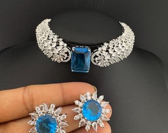May include: A silver choker necklace with a large blue gemstone and smaller white gemstones. Matching earrings with a blue gemstone surrounded by white gemstones.