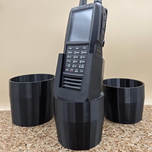 May include: A black two-way radio with a long antenna is in a black charging stand. Two additional black charging stands are on either side of the stand with the radio.