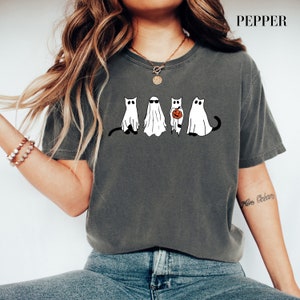 May include: A dark gray t-shirt with a graphic of four cats dressed as ghosts. One cat is holding a pumpkin. The text "Pepper" is in the upper right corner of the image.