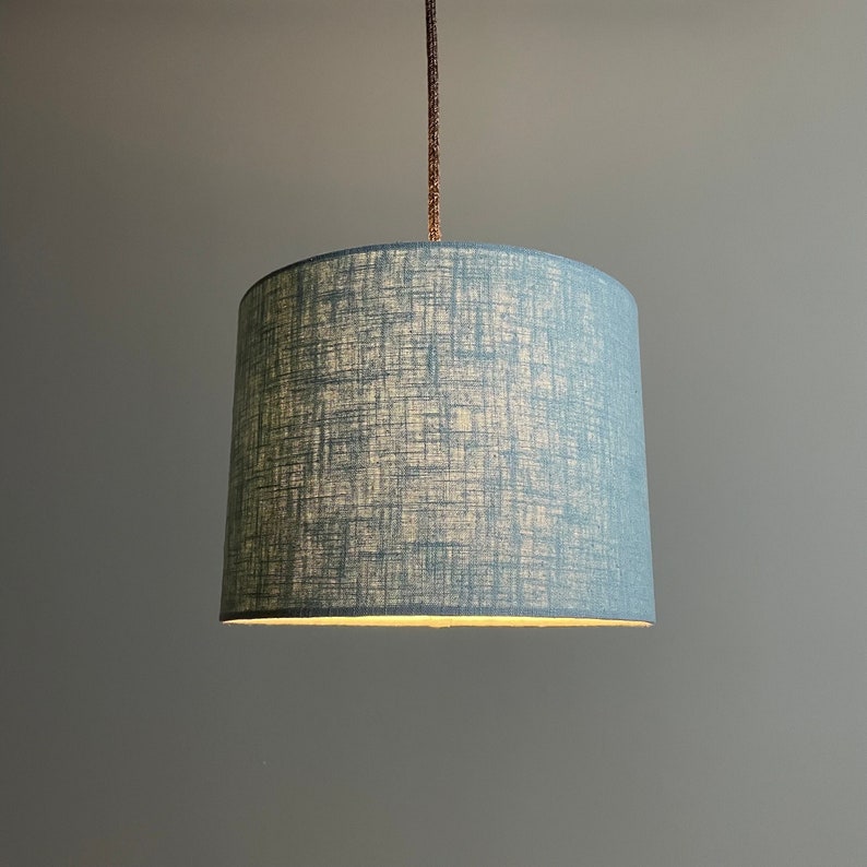 Runder Lampenschirm "Blue Linen" aus 75 % Leinen und 25 % Baumwolle in der Farbe blau/jade. Er hat einen Durchmesser von 24,5 cm und eine Höhe von 18 cm. Er ist für Tischlampen, Hängelampen und Stehlampen geeignet.