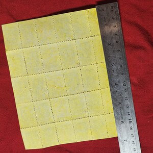 Op de afbeelding: Een vel geel geperforeerd papier met 36 vierkanten, gemeten met een liniaal in centimeters.