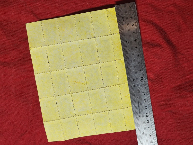 Op de afbeelding: Een vel geel geperforeerd papier met 36 vierkanten, gemeten met een liniaal in centimeters.