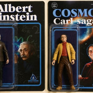 May include: Two action figures in blister packaging. The left figure is Albert Einstein in a brown suit, with his name and a chalkboard background on the card. The right figure is Carl Sagan in a yellow jacket, with the text Cosmos Carl Sagan.