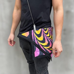 May include: A black t-shirt with a silver chain and a pink, yellow, and black patterned bandana tied around the waist.