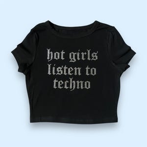 Pode incluir: Camiseta preta de manga curta e corte cropped com o texto "hot girls listen to techno" em strass prateados.