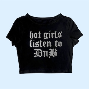 Puede incluir: Camiseta negra de manga corta y corte corto con el texto "hot girls listen to DnB" en pedrería plateada.