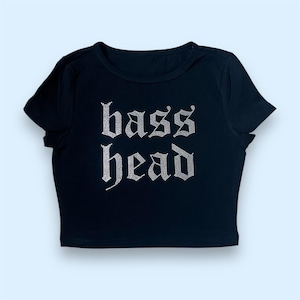May include: Black crop top with the text "bass head" in a rhinestone design. The shirt has short sleeves and a crew neck. The text is in a gothic font.