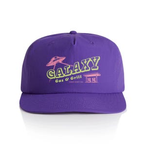 May include: Purple baseball cap with a flat brim. The cap features the text "GALAXY Gas & Grill" in neon green and pink, along with a graphic of a UFO and a gas station. The text "FUGADI COUNTY USA" is also visible.