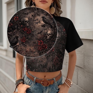 May include: Black crop top with a gothic floral print featuring skulls, roses, and ravens. The design is set against a dark, textured background. The sleeves are solid black.