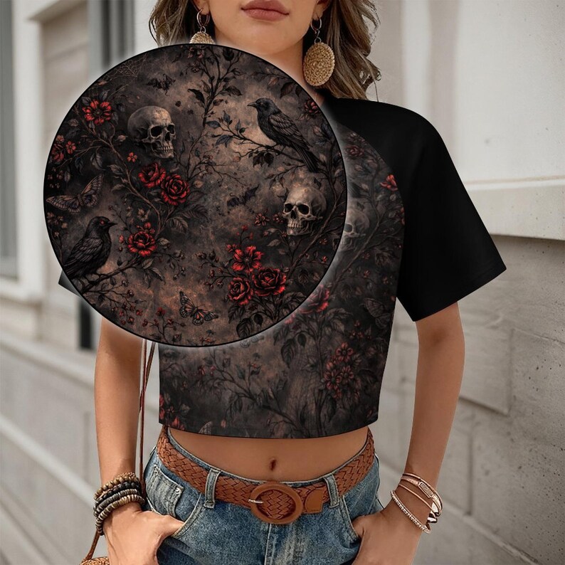 May include: Black crop top with a gothic floral print featuring skulls, roses, and ravens. The design is set against a dark, textured background. The sleeves are solid black.