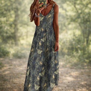 May include: A dark blue maxi dress with a V-neck and spaghetti straps. The dress features a repeating pattern of moths, crescent moons, and leafy vines in shades of green and gold. The dress is floor-length.