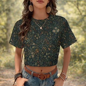 May include: A dark green crop top with a floral pattern in shades of beige, brown, and green. The top has short sleeves and a round neckline. The floral design covers the entire top.