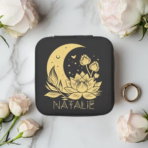 May include: Black jewelry case with a gold crescent moon, lotus flower, and butterfly design. The name "NATALIE" is printed in gold script below the floral design. The case is surrounded by white and pink roses.
