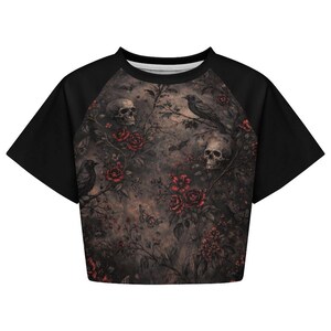 May include: Black crop top with a gothic floral design featuring skulls, red roses, ravens, and butterflies. The sleeves are solid black, and the shirt has a crew neck.