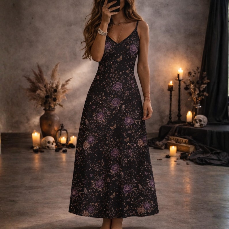 May include: A black maxi dress with a floral pattern in shades of purple and tan. The dress has a V-neck and spaghetti straps. The floor-length dress has a flowing silhouette. The dress is suitable for a special occasion.