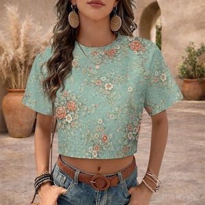 May include: A cropped t-shirt with a floral pattern in shades of peach, white, and green. The shirt has short sleeves and a round neckline. The floral design is set against a light green background.