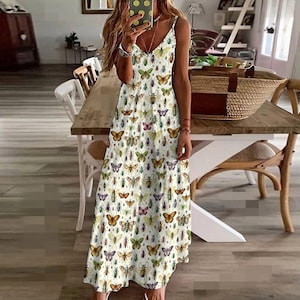 May include: A white, sleeveless dress with a V-neck and spaghetti straps. The dress is covered in a pattern of colorful butterflies and insects. The dress is floor-length.