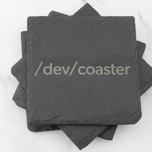 Peut inclure: Un ensemble de quatre sous-verres en ardoise noire avec le texte "/dev/coaster" gravé sur le sous-verre du dessus.