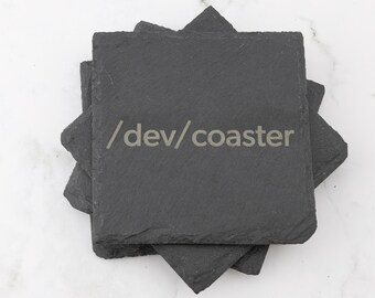 May include: A set of four black slate coasters with the text "/dev/coaster" etched on the top coaster.
