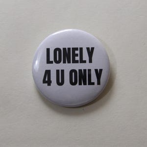 Può includere: Una spilla rotonda bianca con il testo nero LONELY 4 U ONLY stampato in un carattere sans-serif in grassetto. La spilla presenta una finitura liscia e lucida e un design semplice e pulito centrato sulla parte anteriore dell'accessorio.