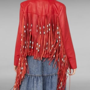 May include: Red leather jacket with fringe and beads. The jacket has a collar and long sleeves. The fringe is on the back of the jacket and hangs down to the waist.