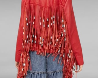 Puede incluir: Chaqueta de cuero roja con flecos y cuentas. La chaqueta tiene cuello y mangas largas. Los flecos están en la parte posterior de la chaqueta y cuelgan hasta la cintura.
