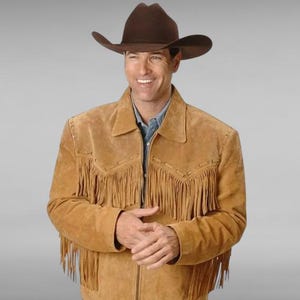 Puede incluir: Una chaqueta de gamuza marrón con detalles de flecos. La chaqueta tiene una cremallera y un cuello de pie. El modelo lleva un sombrero de vaquero marrón.
