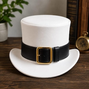 May include: A white top hat featuring a wide black band around the base. The band is secured with a polished gold-tone rectangular buckle centered at the front. The hat has a flat top and a curved brim that extends outward from the base.