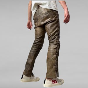 May include: Brown leather pants with a lace-up detail on the sides. The pants are worn with white sneakers.