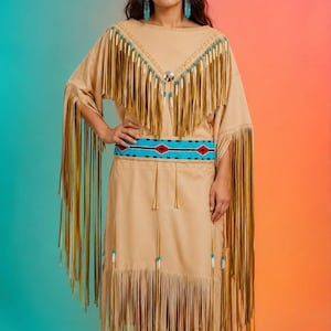 May include: A tan suede-like dress featuring long fringe along the sleeves and hem, a V-shaped yoke with white and tan fringe accents, a central silver concho, and a wide turquoise belt with red and black geometric patterns and matching boots.