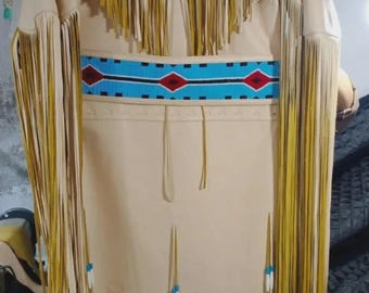 May include: A tan-colored Native American-style dress with long sleeves and fringe detailing. The dress features a beaded belt with red, blue, and black accents. The neckline and sleeves are adorned with fringe and turquoise beads.