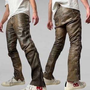 May include: Brown leather pants with a side lace detail. The pants are worn by a person wearing a white t-shirt and white sneakers.