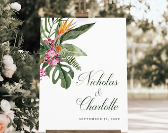 May include: A white wedding sign on a wooden easel, featuring a watercolor floral design with tropical leaves and flowers. The sign displays the names "Nicholas & Charlotte" and the date "September 12, 20XX" in elegant green script.