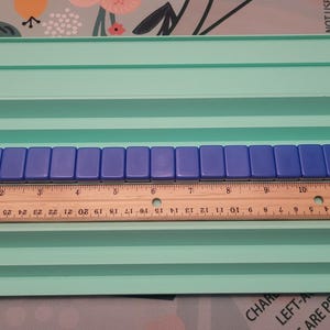 K&ouml;nnte beinhalten: Ein hellgr&uuml;ner Kunststoff-Kachelhalter mit mehreren Ebenen, der blaue Kacheln und ein Holzlineal h&auml;lt. Das Lineal misst bis zu 30 cm. Die Kacheln sind rechteckig und blau.