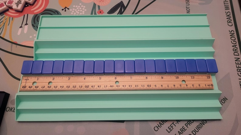 K&ouml;nnte beinhalten: Ein hellgr&uuml;ner Kunststoff-Kachelhalter mit mehreren Ebenen, der blaue Kacheln und ein Holzlineal h&auml;lt. Das Lineal misst bis zu 30 cm. Die Kacheln sind rechteckig und blau.