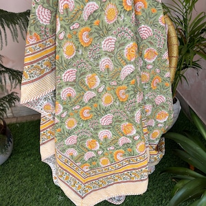 Op de afbeelding: Groene katoenen tafelkleed met een bloemenprint in tinten roze, geel en wit. Het tafelkleed heeft een gele en witte rand.