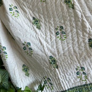 May include: White cotton quilt with a green floral print. The quilt has a border of green and white stripes.