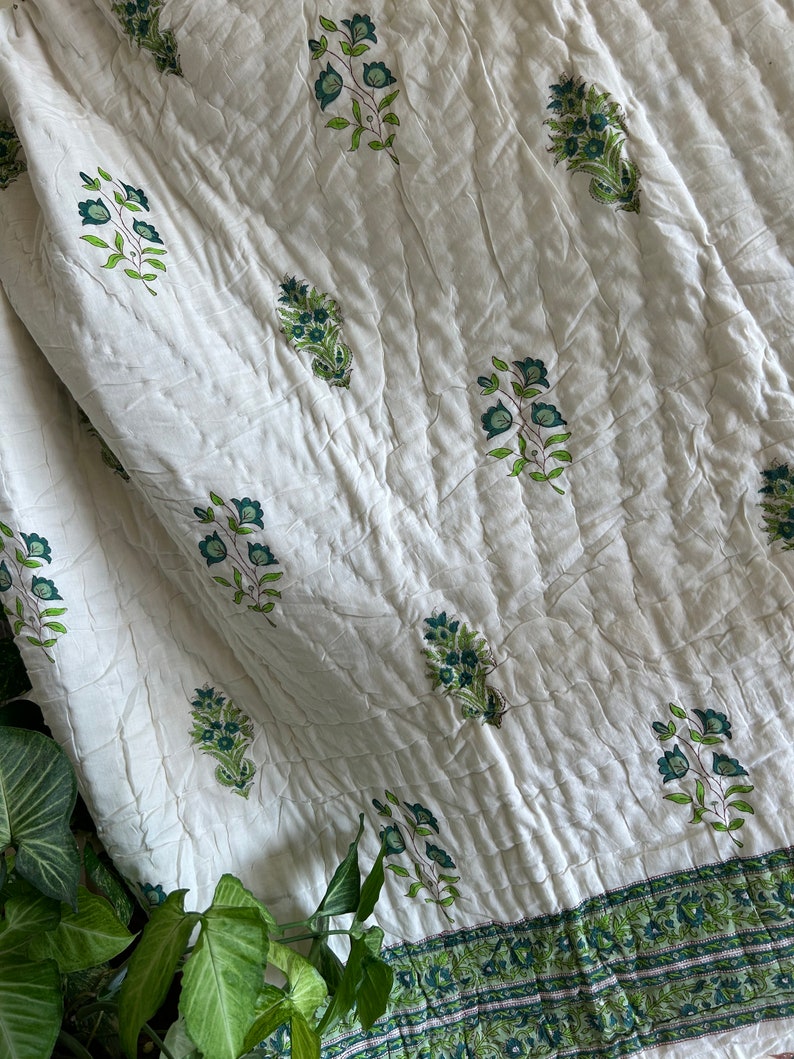 May include: White cotton quilt with a green floral print. The quilt has a border of green and white stripes.