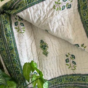 May include: White cotton quilt with a green floral print. The quilt has a border of green and white floral designs. The quilt is folded in half and the floral designs are visible on both sides.