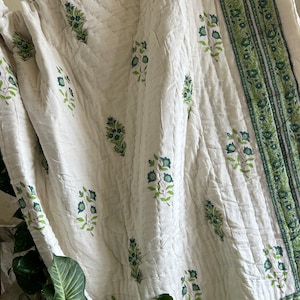 May include: White cotton quilt with a green floral print and a green border. The quilt is folded and draped over a staircase.