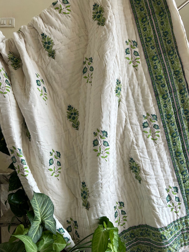 May include: White cotton quilt with a green floral print and a green border. The quilt is folded and draped over a staircase.