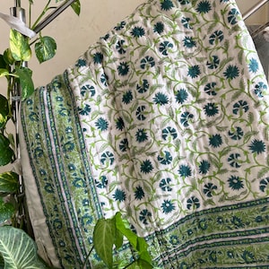May include: White cotton quilt with a green floral pattern. The quilt has a border with a repeating pattern of green leaves and flowers.