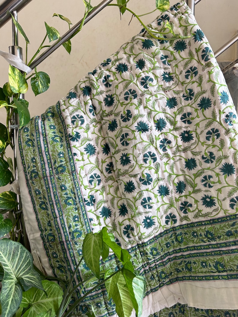 May include: White cotton quilt with a green floral pattern. The quilt has a border with a repeating pattern of green leaves and flowers.