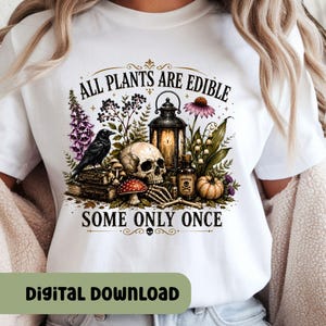 May include: A white t-shirt featuring a graphic print of a skull, a black crow, a lantern, a small bottle labeled poison, a pumpkin, and various plants. The text reads ALL PLANTS ARE EDIBLE SOME ONLY ONCE, with the books labeled Herbal Guide and Garden Secrets.