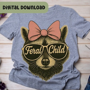 以下が含まれることがあります： 「Feral Child」の文字が入ったサングラスとピンクのリボンをつけたアライグマが描かれたグレーのTシャツ。「Digital Download」の文字がTシャツの上部にあります。