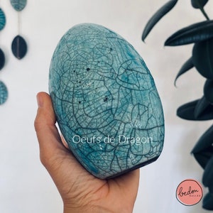 Pode incluir: Um ovo de cerâmica azul turquesa com um esmalte craquelado e o texto "Oeufs de Dragon" no lado.